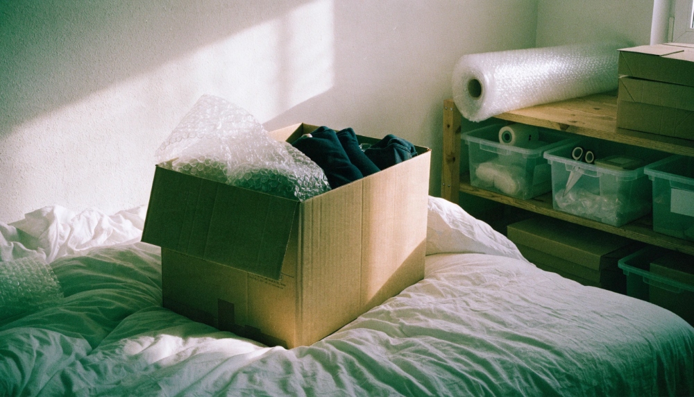 Offener Umzugskarton beim Packen auf dem Bett neben der Packstation